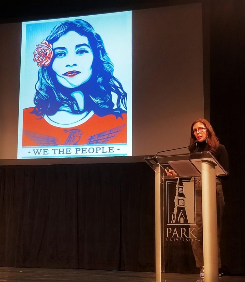 Paola Mendoza standing on stage with a poster of a woman with a flower in her hair speaking about the influence art had on the Womens March on Washington D.C.