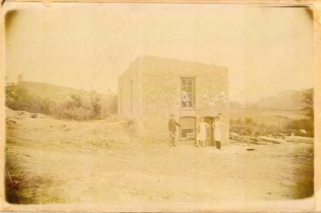 Old photograph from the late 1800s. Three people stand in front of the old bakery building.