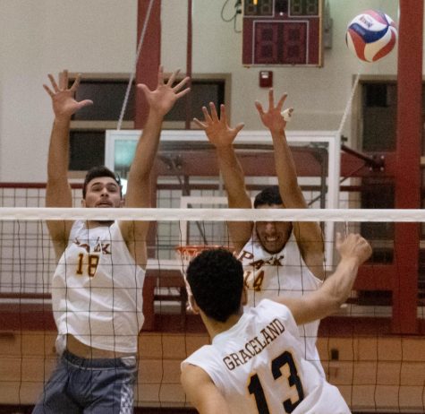 Felipe Chagas and Caio Alves jump with their arms reached upwards to try to block the volleyball that is being spiked towards them by a Graceland University player.